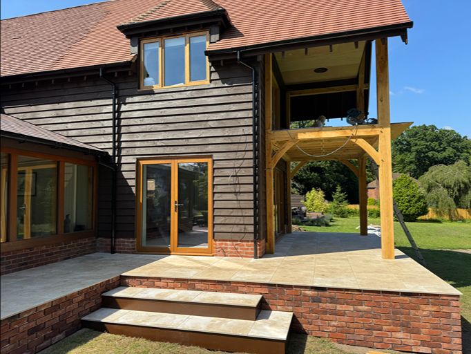 Raised porcelain patio with oak pergola and brick retaining wall