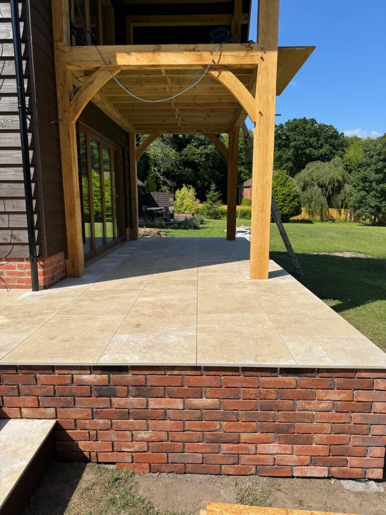 Raised porcelain patio with oak pergola and brick retaining wall